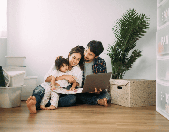 Young couple using laptop with their daughter on the floor of their new home