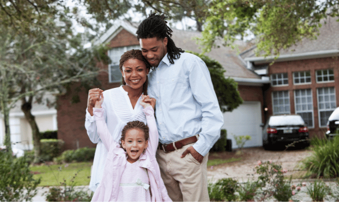 Happy family of 3 standing in front of their new home