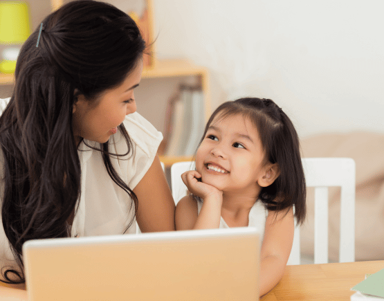 Mother smiling at her young daughter while using a laptop