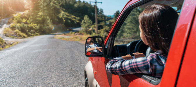 young woman leaning out of red jeep window looking at open road